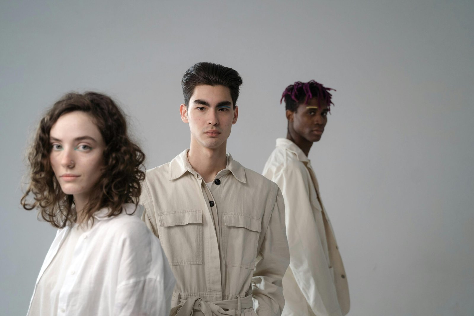Group of diverse multiethnic young people wearing light beige and white cotton clothes standing in studio and looking at camera on gray background