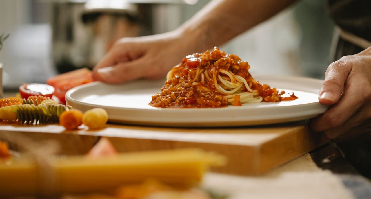 Home Crop anonymous chef taking portion of delicious pasta with sauce while cooking lunch in kitchen